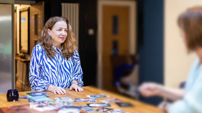 Maxine, founder of Max Purpose Psychology, smiling and holding a card during a supervision or coaching session with a client, seated at a table with visual cards and resources.