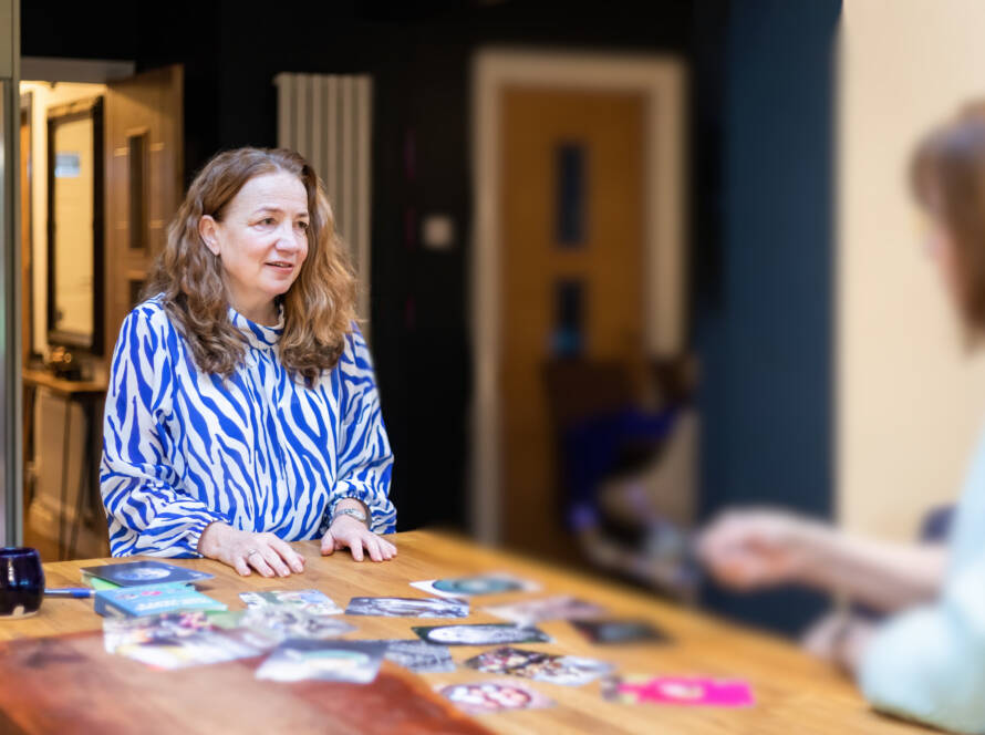 Maxine, founder of Max Purpose Psychology, smiling and holding a card during a supervision or coaching session with a client, seated at a table with visual cards and resources.