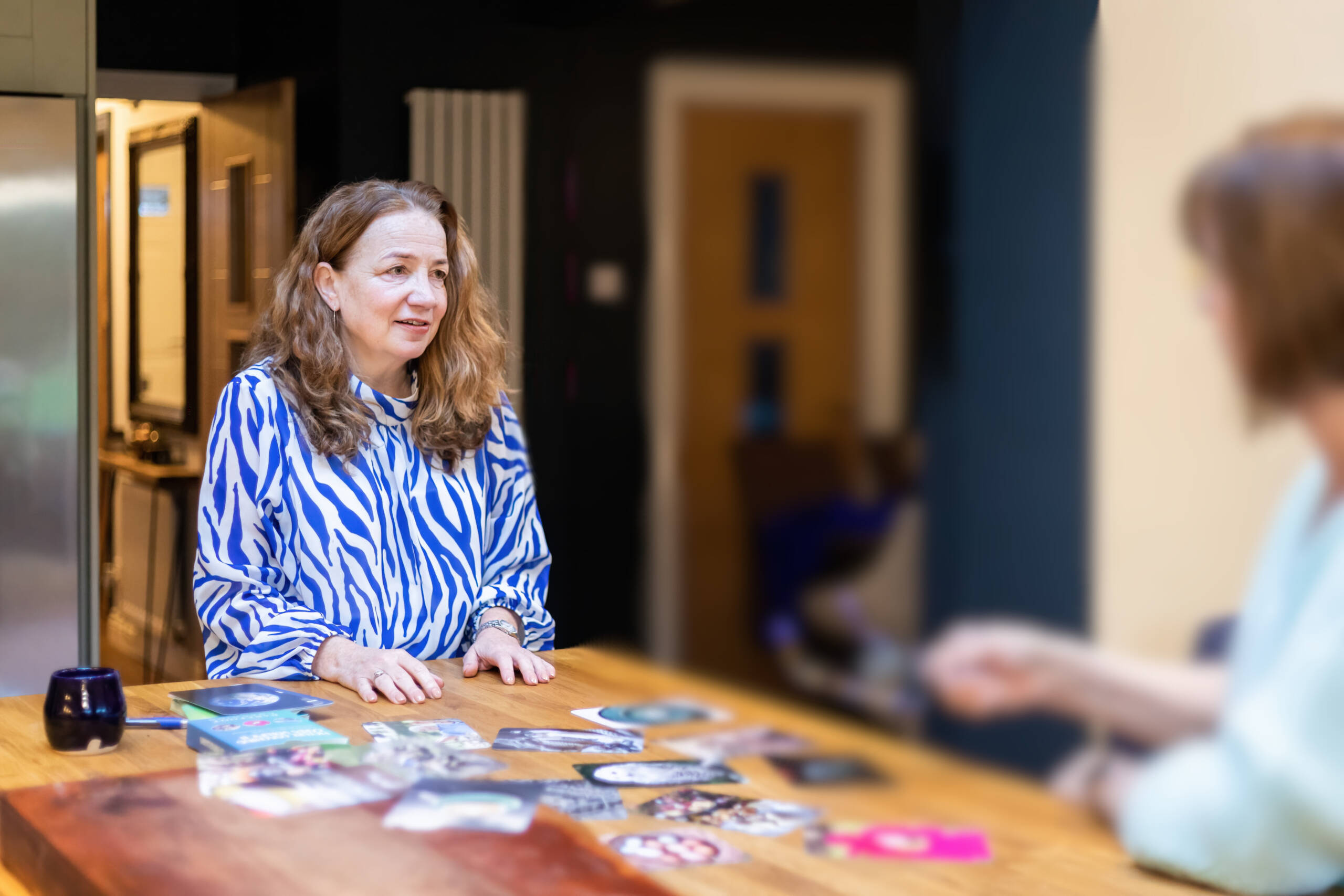 Maxine, founder of Max Purpose Psychology, smiling and holding a card during a supervision or coaching session with a client, seated at a table with visual cards and resources.