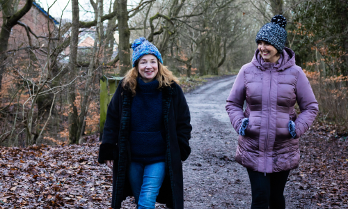 Maxine and a female client walk down a country road in winter during a 1-1 coaching session, they are wearing woolly hats and there are no leaves on the trees.