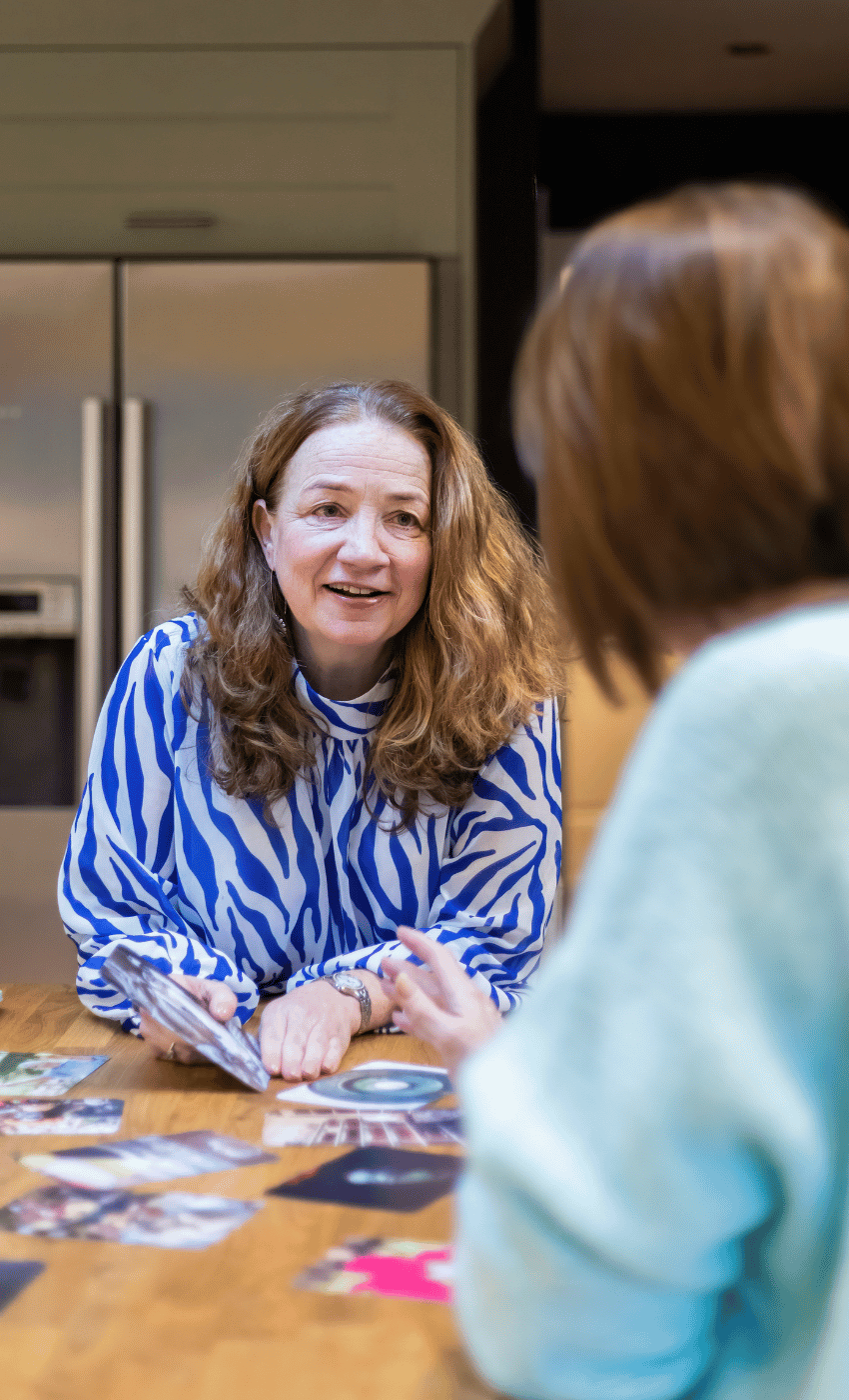 Maxine, founder of Max Purpose Psychology, smiling and holding a card during a supervision or coaching session with a client, seated at a table with visual cards and resources.